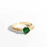 Anillo dorado con cristal verde esmeralda en el centro y pequeños cristales claros alrededor.