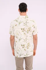 Camisa blanca con estampado de hojas verdes y marrones, de manga corta y cuello clásico.