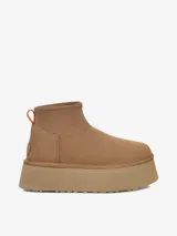 Bota corta tipo botineta con plataforma elevada, confeccionada en gamuza color tostado. Presenta un diseño minimalista con cuello elástico y una pequeña presilla naranja en la parte posterior.
