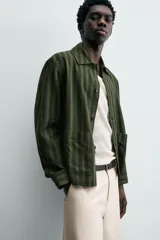 Sobrecamisa de hombre con cuello solapa, manga larga y cierre frontal de botonadura. Presenta un estampado de rayas verticales en tonos de verde oliva y verde oscuro. Incluye bolsillos plastrón en la cadera.