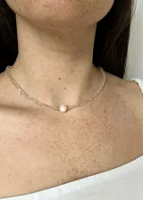 Gargantilla de cristales facetados color rosa claro con cierre de mosquetón dorado y perla de río central.