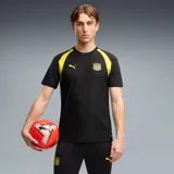 Camiseta de fútbol Puma Cap Tr. Jersey, de color negro con detalles en amarillo en los hombros y cuello. Presenta un sutil diseño gráfico en relieve sobre el tejido y el logo de la marca junto al escudo del Club Atlético Peñarol en el pecho.