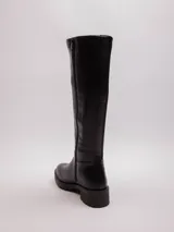 Bota de caña alta color negro, de símil cuero con pieza elástica en la parte trasera de la caña y cierre lateral. Cuenta con plataforma dentada.