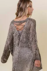 Buzo de tejido liviano y calado con brillo sutil, color gris oscuro o negro. Presenta un calce amplio y mangas amplias, con un detalle de tiras entrelazadas en la espalda. El largo es irregular, más largo en la parte trasera.