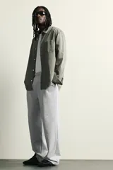 Pantalón jogger de corte relajado y pernera ancha, confeccionado en tejido de algodón con interior perchado. Cuenta con cintura elástica ajustable mediante cordón interior, bolsillos laterales y un bolsillo trasero de plastrón.