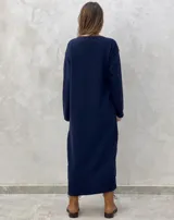 Vestido midi de punto color azul marino, con cuello en V, mangas largas y diseño holgado. Presenta un patrón de rombos en relieve y aberturas laterales con botones decorativos en el ruedo.