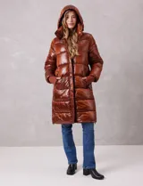 Campera puffer larga de abrigo marca BCBG Maxazria, color beige. Cuenta con capucha desmontable, cuello alto envolvente, cierre frontal bidireccional con solapa de botones a presión, bolsillos laterales, puños internos elastizados y tajos laterales con cierre en el bajo.