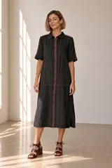 Vestido midi chemise de lino color beige, con cierre frontal de botones, cuello camisero, mangas cortas con vuelta y detalles en marrón oscuro en la botonera y los hombros.
