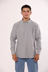 Camisa de manga larga en color gris, confeccionada en algodón, con cuello abotonado y cierre frontal de botones.