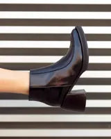 Botas de cuero negras con punta cuadrada, tacón ancho y detalles de textura en relieve en la parte superior.