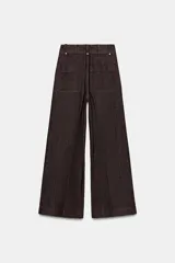 Jeans de tiro alto confeccionados en mezcla de algodón, con diseño de pierna ancha y costura marcada en el delantero. Presenta cintura con trabillas, cierre frontal con cremallera, botón y gancho metálico, y bolsillos de plastrón en la espalda.