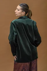 Blazer de terciopelo en color verde profundo, con solapas anchas, cierre frontal con un botón y bolsillos laterales con solapa. Presenta un corte relajado y estructura fluida.