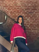 Buzo de tejido de punto con diseño a rayas horizontales en tonos fucsia y rojo. Presenta cuello redondo, puños y ruedo en color crudo, con un corte holgado y relajado.