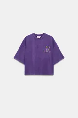 Camiseta corta de efecto lavado, de color morado, con cuello redondo, manga corta y detalle de texto multicolor a contraste en el pecho. Colección especial Fruit of the Loom y Zara.