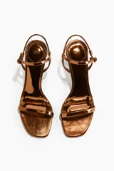 Sandalias de tacón alto fino con acabado metalizado dorado, diseño de tiras finas y tira ajustable al tobillo con hebilla.