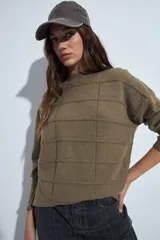 Sweater de punto gris con cuello a la base y diseño de trama geométrica en relieve. Presenta un calce relajado con mangas largas y puños tejidos.
