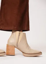 Botín de cuero color beige con textura reptil, elástico lateral y cierre interno. Tiene plataforma delantera y taco de madera.