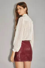 Falda corta cruzada de cuero ovino color bordó, con tachas metálicas plateadas decorando el borde y la cintura.