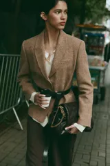 Blazer de corte clásico con cuello solapa y manga larga, confeccionado en tejido con patrón de espiga en tonos tierra y líneas verticales en color salmón. Cuenta con bolsillos delanteros y cierre frontal con botones ocultos.