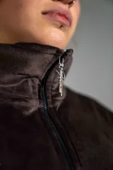 Buzo de plush color marrón, con cuello alto y cierre frontal parcial. Presenta un diseño holgado con puños elásticos y un pequeño bordado en el pecho.