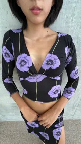 Top de lycra con escote en V profundo y mangas tres cuartos. Presenta un diseño estampado de flores violetas sobre fondo negro con líneas verticales finas en color amarillo.