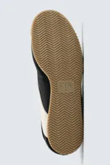 Zapatilla de estilo retro con cordones, confeccionada en una combinación de piezas de cuero sintético negro y detalles en blanco, con suela dentada de goma en tono caramelo.