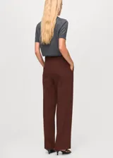 Pantalón de vestir marrón de tiro alto y diseño recto, con bolsillos laterales y cierre oculto con botón, gancho y cremallera.