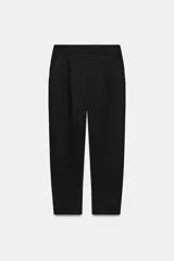 Pantalón de tiro medio con pinzas delanteras, bolsillos laterales y falsos bolsillos de vivo en la parte trasera. Presenta un corte holgado que se estrecha hacia el tobillo, con bajo acabado en pliegues y cierre frontal con cremallera, botón interior y gancho.