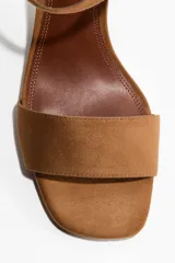 Sandalias de gamuza color marrón tostado, con taco de bloque medio, punta cuadrada, tira delantera ancha y tira al tobillo con hebilla metálica dorada.