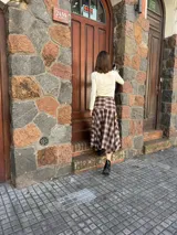 Pollera midi de corte amplio con estampado escocés en tonos marrones. Presenta un diseño distintivo con un detalle de atado en la cintura que simula puños de camisa y cierre frontal con botones.