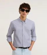 Camisa de vestir de hombre, corte regular, confeccionada en tejido Oxford rayado en tonos azul y blanco. Cuenta con cuello abotonado, manga larga con puños abotonados y cierre frontal con botones.