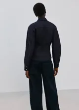 Camisa de denim azul oscuro, con cuello camisero, cierre frontal con botones y mangas largas ajustadas.