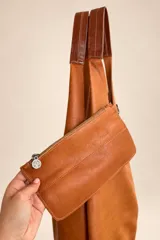 Bolso tipo tote de gamuza azul marino, de gran capacidad y diseño flexible, con asas largas de cuero marrón oscuro y placa metálica con la marca grabada en la parte frontal.