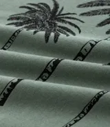 Remera verde oliva de algodón, corte comfort, cuello redondo y manga corta. Estampado frontal con tres palmeras negras y texto inferior.