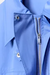 Vestido corto de estilo camisero color azul, con cuello solapa, manga corta y cierre frontal con botones. Presenta un bolsillo de plastrón con solapa en el pecho y un cinturón ajustable del mismo tejido en la cintura.