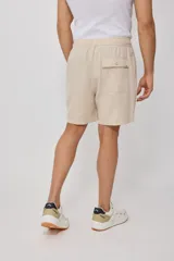 Bermuda de corte recto en color beige, confeccionada en una mezcla de algodón, lino y poliéster. Presenta cintura elástica con cordón ajustable, bolsillos laterales y una pequeña etiqueta decorativa en el ruedo.