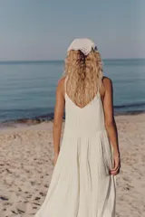 Vestido largo satinado color crudo, con escote en pico adornado con lazada y tirantes finos ajustables. Presenta detalles de frunces y diseño fluido.
