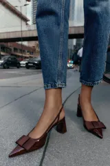 Zapato destalonado de mujer, color borgoña (vino), con acabado acharolado y punta fina. Presenta un lazo de tela en la parte delantera y una tira fina en el talón. El tacón es ancho y de altura media.
