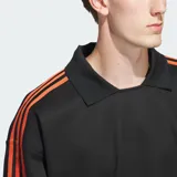 Camisa polo Adidas de manga larga en color negro, con cuello clásico y las icónicas tres tiras naranjas en las mangas. Presenta el logotipo del trébol bordado en naranja en el pecho con la inscripción 'Basketball'.