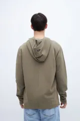Canguro verde oliva de felpa liviana teñido en prenda, con capucha, bolsillo tipo canguro y puños acanalados. Estampa con la leyenda "UNFRM-STATE" en el pecho y detalle de estampa en la manga. Corte recto.