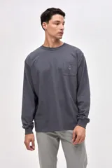 Remera de manga larga en color gris oscuro, confeccionada en algodón pesado con textura suave. Presenta un bolsillo frontal en el pecho con un pequeño bordado de la marca y puños elásticos en las mangas.