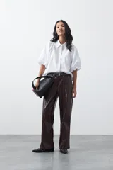 Pantalón de cuero sintético en color marrón oscuro, con corte flare, tiro medio y costuras frontales verticales que estilizan la silueta.