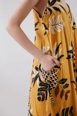 Vestido largo amarillo con estampado de hojas de palmera en blanco y negro, con breteles finos y botones en el frente.
