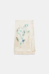 Falda midi de tiro medio con estampado floral en tonos azules y verdes sobre fondo beige. Presenta una abertura frontal en el bajo y cierre lateral con cremallera oculta.