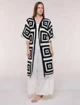 Cardigan largo confeccionado en tejido de punto calado estilo crochet, de color amarillo y blanco, con diseño geométrico de cuadrados, mangas amplias tipo kimono y corte abierto al frente.