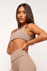 Top deportivo color beige con contorno negro, breteles anchos y logo pequeño en el frente.