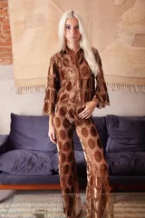 Pantalón de corte evasé confeccionado en tela calada con círculos de terciopelo color marrón. Presenta cintura elástica con cierre para mayor ajuste y comodidad.
