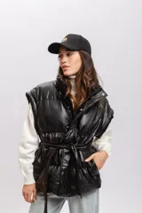 Chaleco negro puffer de cuero sintético con cuello alto y cierre frontal con botones a presión. Incluye cinturón de lazo del mismo material.