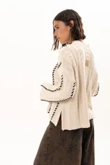Buzo tejido de punto con silueta relajada, cuello alto y mangas tipo campana. Presenta un diseño de trenzas verticales con detalles de costuras en contraste a lo largo de la prenda.
