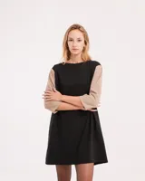 Vestido corto negro con mangas 3/4 verdes, cuello bote y bolsillos laterales.